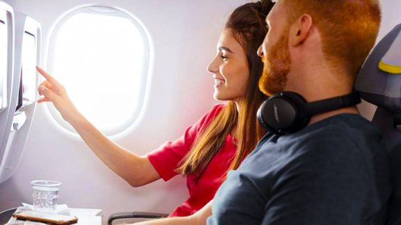 یک مرد و یک زن که مرد از هدفون شخصی مشکی رنگ استفاده میکند و با هم از سیستم تصویری هواپیما فیلم نگاه میکنند.